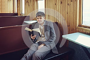 young man in a vintage railway car is sitting reading a book and looking out the window