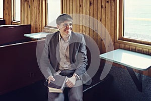 young man in a vintage railway car is sitting reading a book and looking out the window