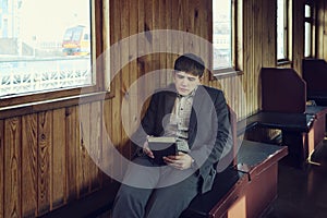 young man in a vintage railway car is sitting reading a book and looking out the window