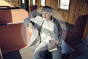 young man in a vintage railway car is sitting reading a book and looking out the window