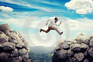 Young man in virtual reality headset jumping between two high rocks