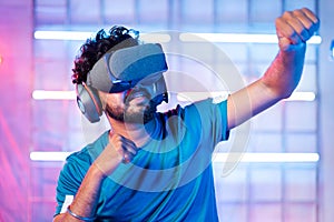 Young man with VR or virtual reality goggles or headphones dancing on neon light staged backgound - concept of modern
