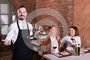 Young man waiter demonstrating country restaurant