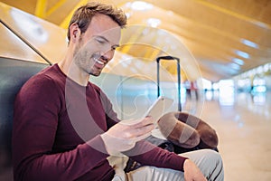 Young man waiting using mobile phone at the airport with a suitcase