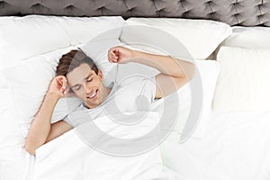 Young man waking up in bed with pillows
