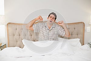 Young man waking up in bed and stretching his arms