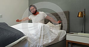 Young man waking up in bed and stretching his arms