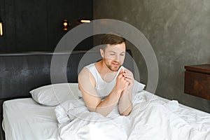 Young man waking up and rise hands stretching on white bed in the morning with sunlight through window