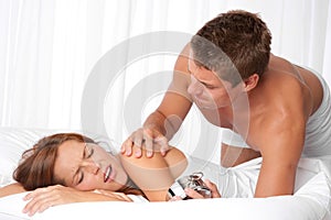 Young man waking up woman in white bed