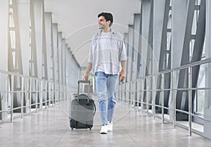 Young man walking in airport walkway with luggage photo