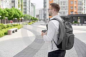 Young man walking with backpack and coffee cup in city. photo