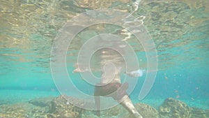 Young man walking in blue clear under water of waterfall with many rocks from flat angle