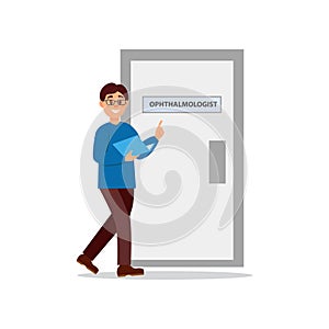 Young man walking at doctor s office. Door of ophthalmologist cabinet. Guy in glasses, blue sweater and brown pants with