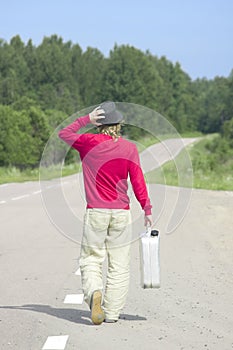 Young man walking down highway with empty gas can
