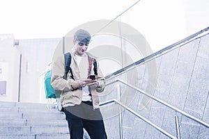 Young man walking down stairs with backpack while using mobile outdoors