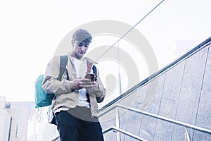 Young man walking down stairs with backpack while using mobile outdoors