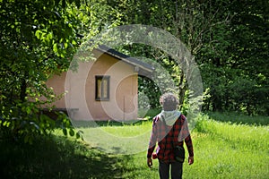 Young man walking in the green towards a pink cottage