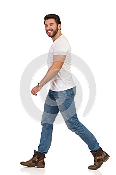Young Man In Jeans And White T-shirt Is Walking And Looking At Camera. Side View