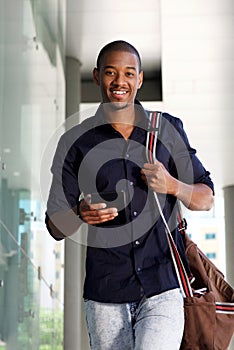 Young man walking outside with mobile phone and bag