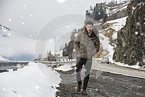 Young man walking on roadside under the snow