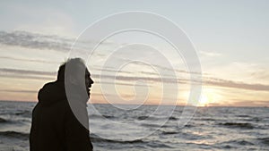 Young man walking in the shore of the sea alone and looking on the waves. Male enjoying the sunset on the beach.