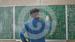 Young man is walking to blackboard wall in college class looking at formulas thinking about science. Education, people