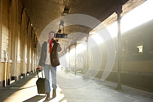 Young man walking at train station with bag and mobile phone