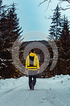 Young man walking on winter czech forest path in yellow jacket