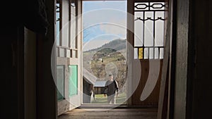 A young man walks through the open door of the house. View from inside.