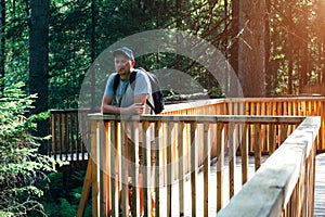 A young man walks through the park. A man with a backpack on his shoulders stands thoughtfully looking at the forest