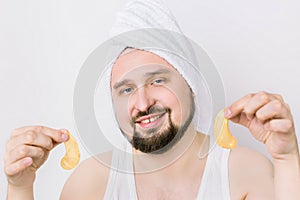 Young man wants to look fresher and caring about his skin. Handsome bearded guy in towel on head holds golden anti