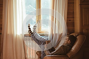 Young man in warm sweater reading by the window inside cozy log cabin photo