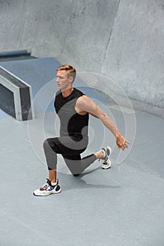 Young Man Warming Up Against Concrete Wall Outdoors. Handsome Caucasian Sportsman With Strong Muscular Body.