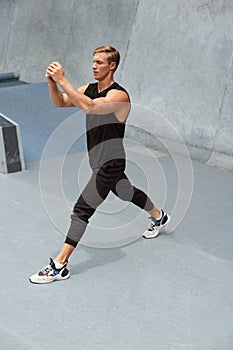 Young Man Warming Up Against Concrete Wall Outdoors. Handsome Caucasian Sportsman With Strong Muscular Body.