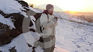A young man warms his frozen hands with his breath in the winter at sunset.