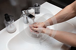 A young man washes his hands with soap in the bathroom. Compliance with hygiene. Take care of your health.