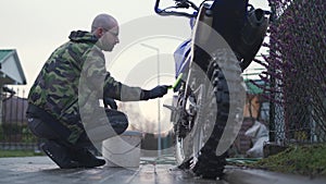 Young man washes motocross by hand, using a brush and hosepipe