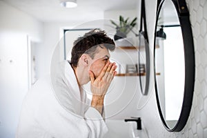 Young man washing face in the bathroom in the morning, daily routine.