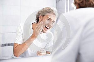 Young man washing face with soap near mirror