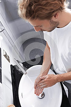 Young man washing hands with soap over sink