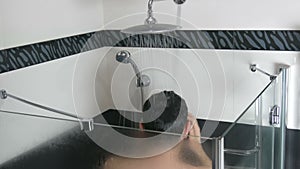 A young man is washing himself under the shower. Washing your hair under running water in the shower in the morning or