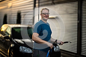 Young man washing his beloved car carefully in a manual car wash