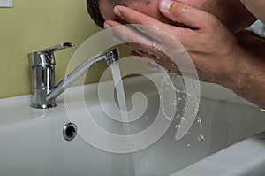 Young man washing his face in the bathroom in the morning