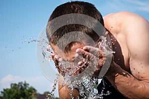 Young man washing his face with water on a blue sky background