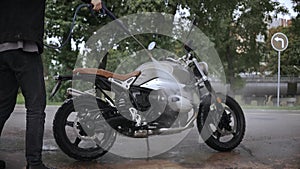 Young man washing his scrambler motorbike with water hose on the street