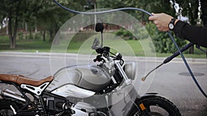 Young man washing his scrambler motorbike with water hose on the street