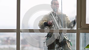 Young man washing wide window with magnetic cleaning brush on the background of blurred city