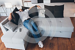 Young man watch tv in his own apartment. Picture of guy in deep sleep or daydream. Sitting or lying on couch and hold
