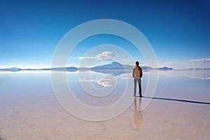 Young man watching the scenery and miror effect in Salar de Uyuni Uyuni salt flats, Potosi, Bolivia South America