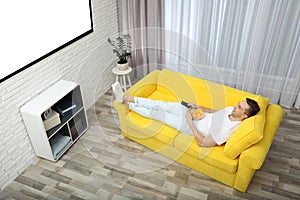 Young man watching TV and eating chips on sofa at home, above view.